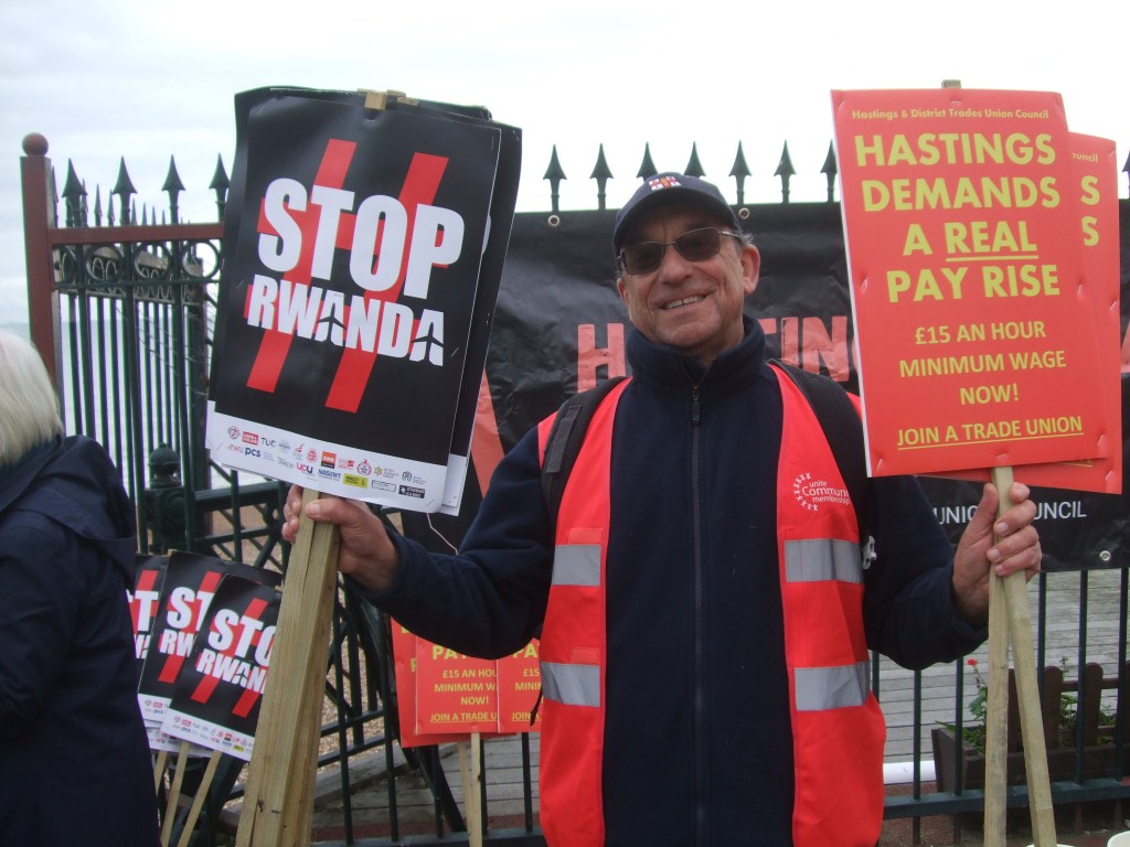 H TUC chair with 'Stop Rwanda' and 'Hastings Deserves a Pay Rise' placards